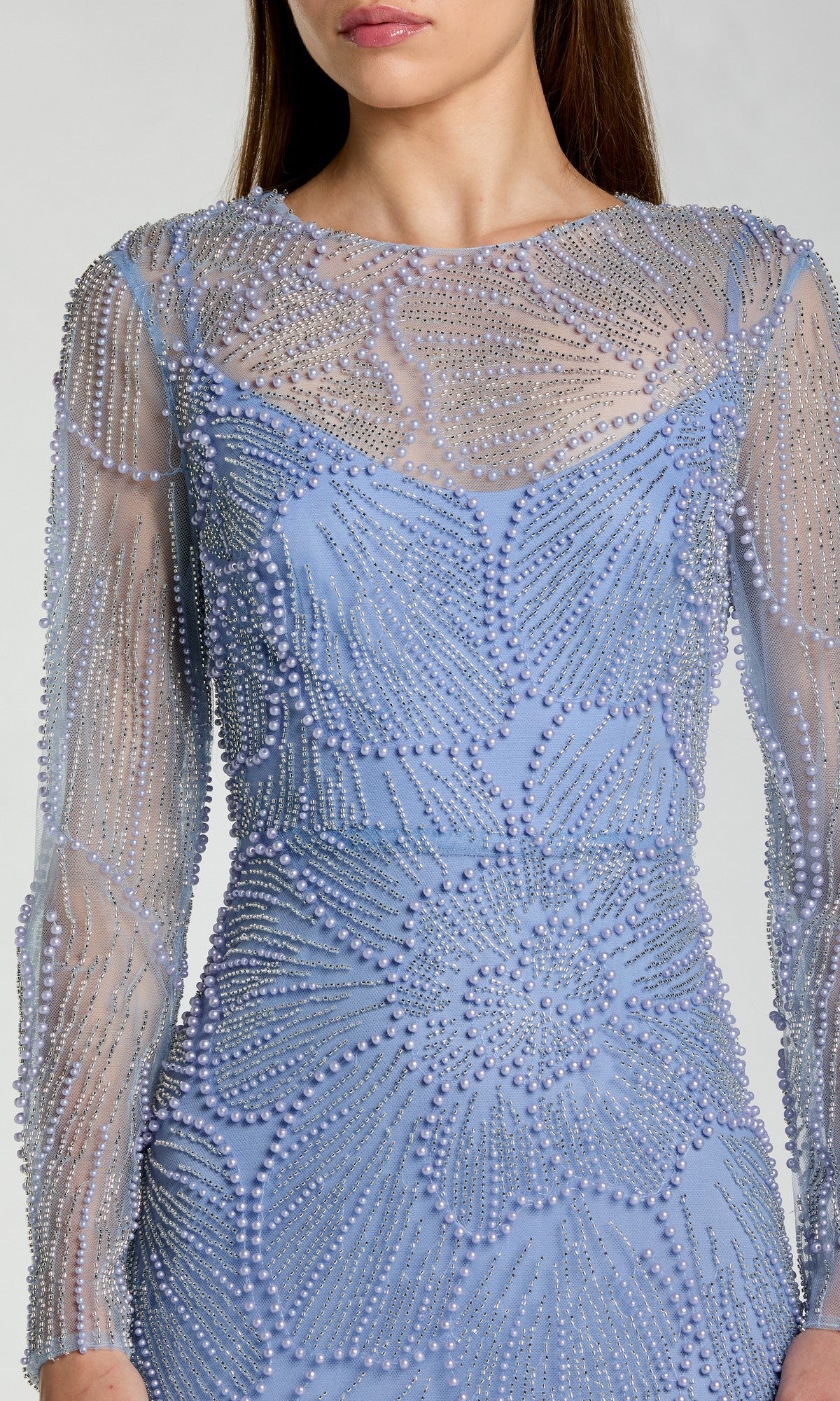 A woman wearing the Mac Duggal 69012 Long Formal Dress, featuring sheer long sleeves and intricate beaded embellishments in elegant floral patterns—a perfect choice for those seeking a modest, lavender evening gown.
